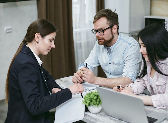 a-couple-sitting-down-with-another-person-discussing-tenant-screening-at-a-desk